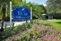 The Tot Lot sign and flower bed with play equipment in the background.